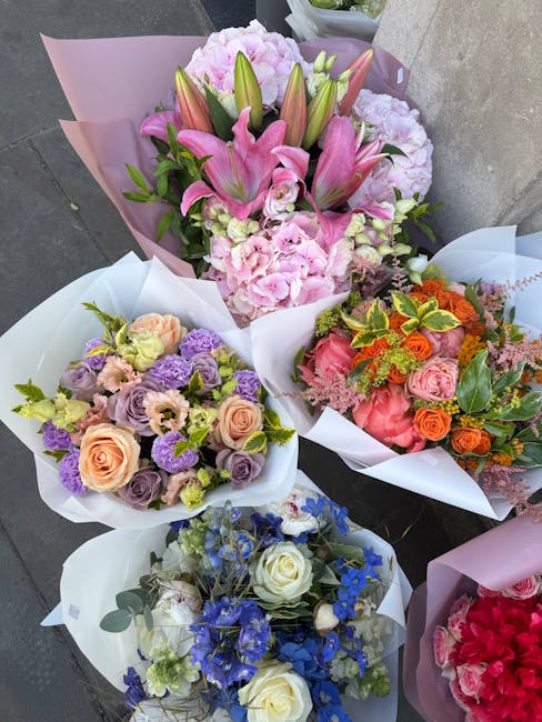 A collection of four floral bouquets arranged in white wrapping paper, displayed on a grey surface. The top bouquet features pink lilies, pale pink hydrangeas, and greenery, wrapped in pink paper. The