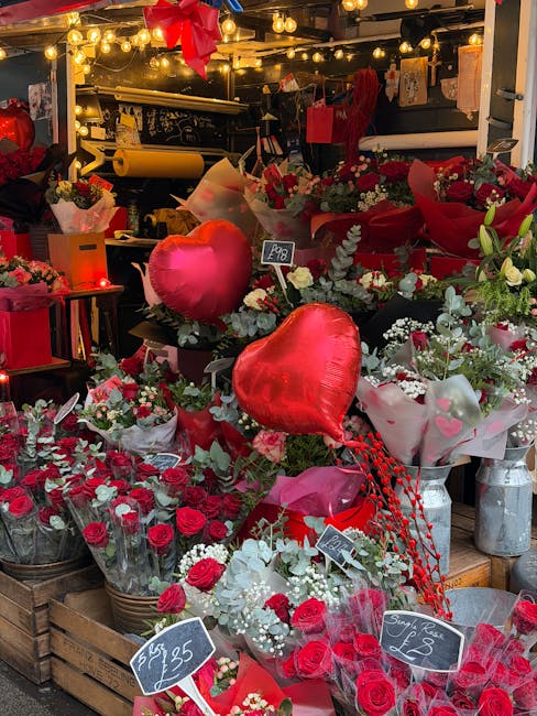A display of floral arrangements featuring a variety of red and white roses, white lilies, and greenery, arranged in bouquets wrapped in tissue paper and placed in baskets and vases at a flower shop. 