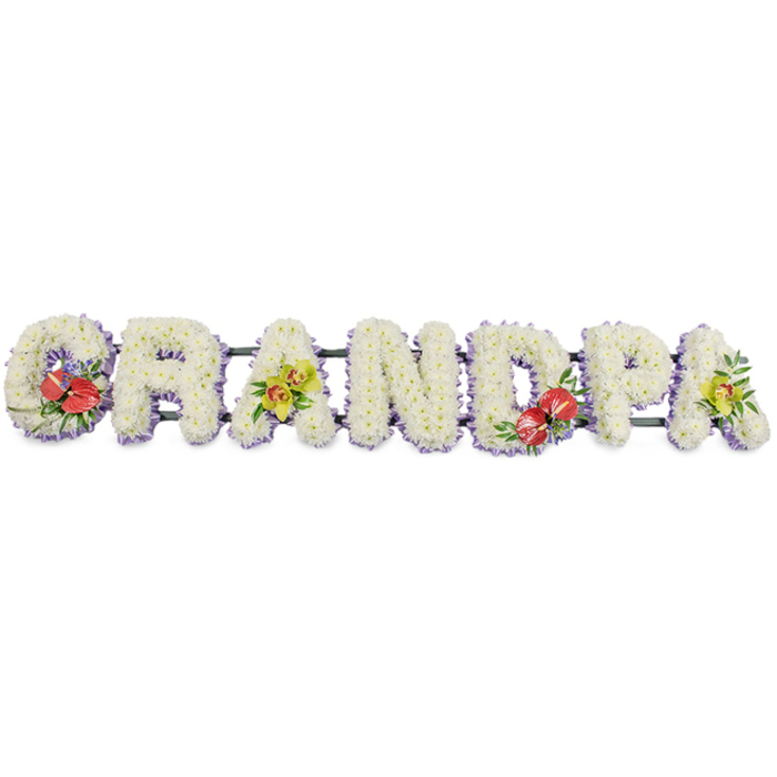 A beautifully balanced floral tribute forms the word "GRANDPA" in large, upright block letters, the kind of piece you might see resting near the front of a chapel in Muswell Hill during a heartfelt farewell. Each individual letter is entirely clothed in tight clusters of fresh white chrysanthemums, creating a thick, cushion-like surface that is soft to the eye and rich in texture, conveying purity, peace, and quiet affection. Around the lower edge of every letter, a slim band of lavender ribbon adds a defined border; its muted lilac tone brings a gentle contrast to the white blooms and echoes the cool, calm palette often seen in elegant North London funeral flowers. Behind the letters, dark green bars run discreetly along the length of the tribute, connecting and supporting the design so it can be placed on a stand beside the coffin or at the graveside. Thoughtfully positioned sprays of accent flowers bring colour and personality to this memorial. On the 'G' and 'D', clusters of deep red anthuriums, with their smooth, waxy heart-shaped spathes and pronounced yellow spadices, are framed by lush green foliage and hints of purple filler blooms, creating dramatic focal points. On the first and last 'A', sprays of yellow-green orchids, with slender petals and intricate centres, soften the tribute and symbolise enduring love and admiration. Crafted with the sensitivity of a local florist who understands family traditions across Muswell Hill, Highgate, and nearby streets around Colney Hatch Lane, this personalised "GRANDPA" arrangement offers a dignified, expressive way to honour a grandfather's life at a funeral, wake, or memorial gathering.